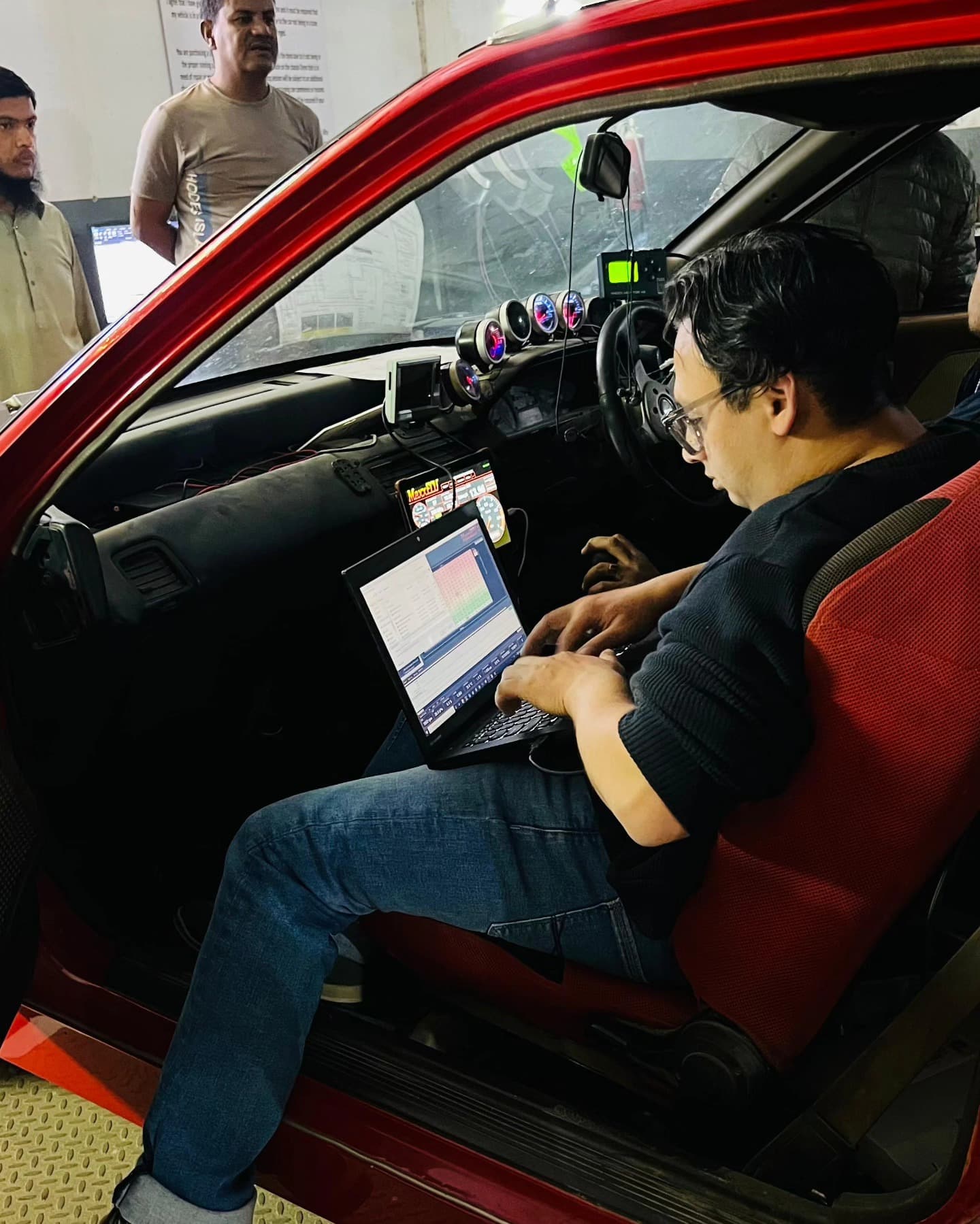 Live ECU tuning session inside the Honda EF K24 AWD turbo Civic, laptop on lap with gauges and standalone ECU wiring visible